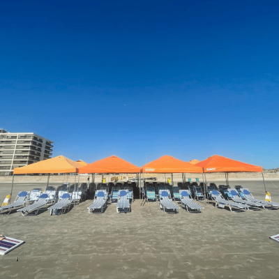 Orange tents and beach chairs on a sandy beach under a clear blue sky.
