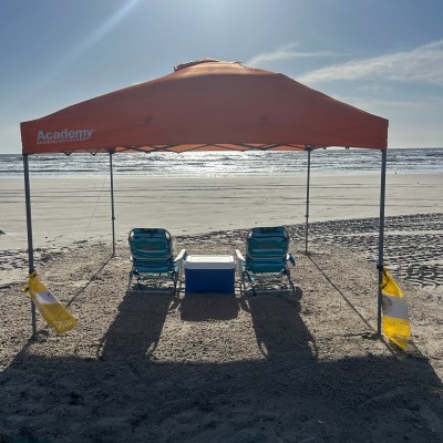 Beach canopy with two chairs, cooler, under sunny sky.