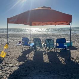 Beach scene with chairs under an orange canopy facing the ocean.
