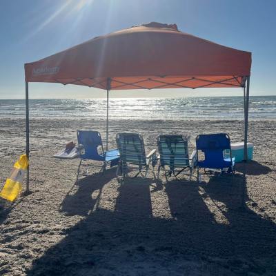 Beach scene with chairs under an orange canopy facing the ocean.