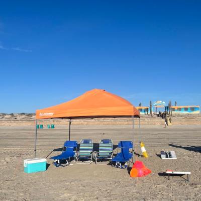 Orange tent and four chairs on a sandy beach with blue sky.