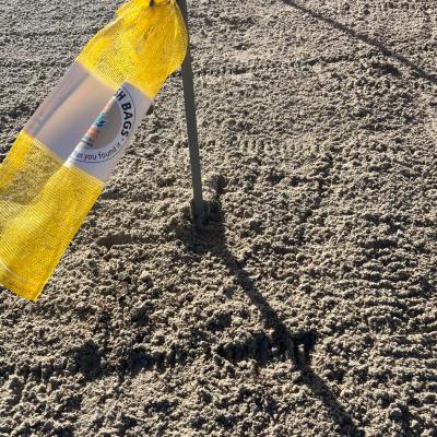 Yellow mesh bag hanging on a pole in sandy terrain.