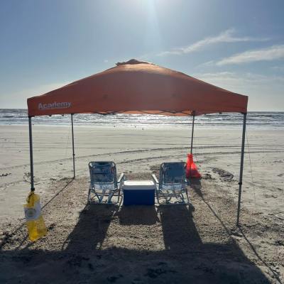 Beach scene with orange canopy, two chairs, cooler, and sunlight.